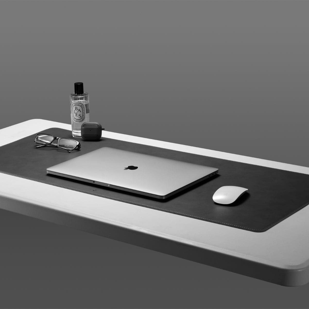 APP04762 - LD302 Desk Pad in black showing the desk pad on a white table with laptop, mouse and glasses on top