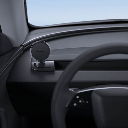 ACP11873 - Spigen magnetic phone mount folded down on a car dashboard near the steering wheel, showing the Spigen logo on the magnetic plate